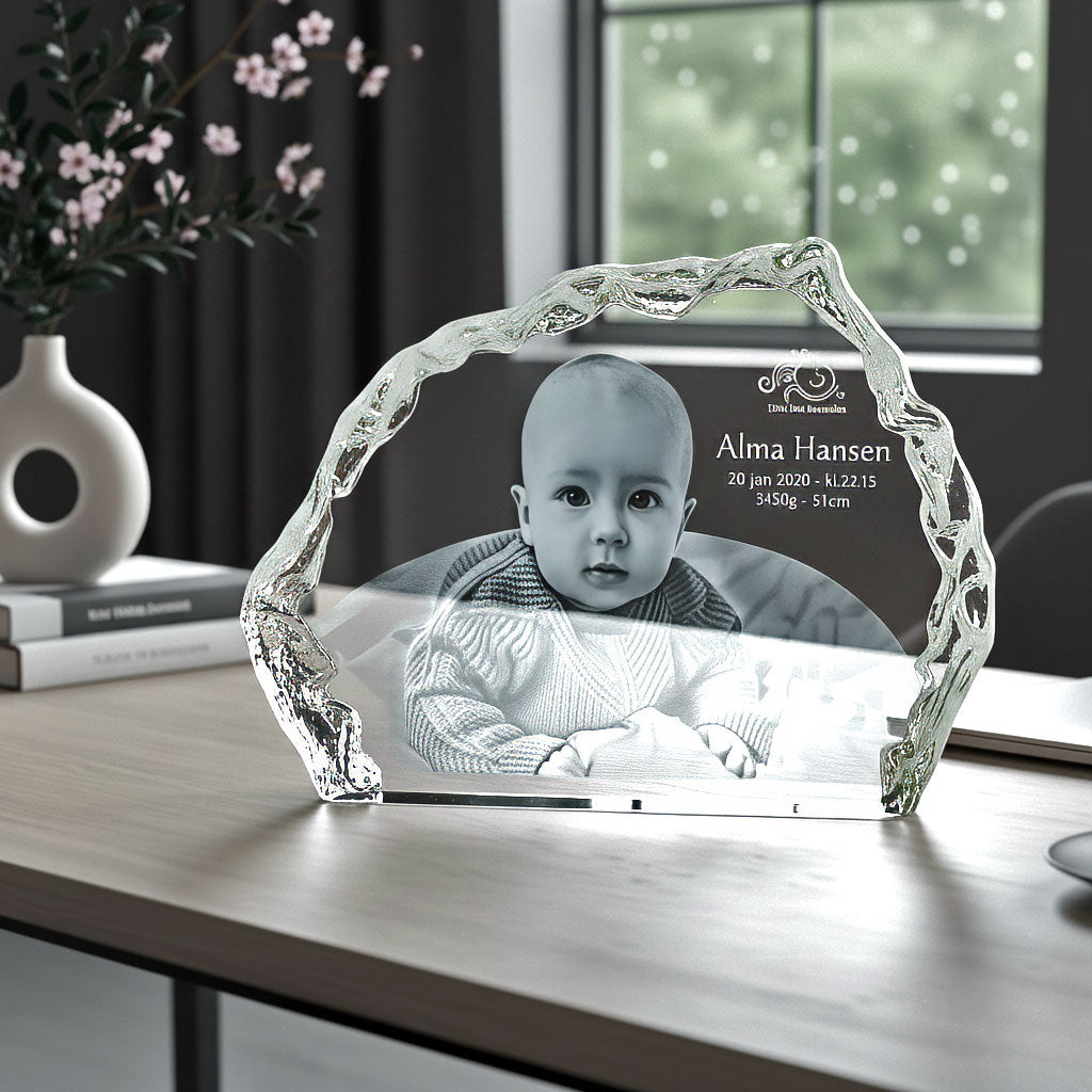 Isbergsformad glasblock med graverad bebis på ett skrivbord vid fönstret