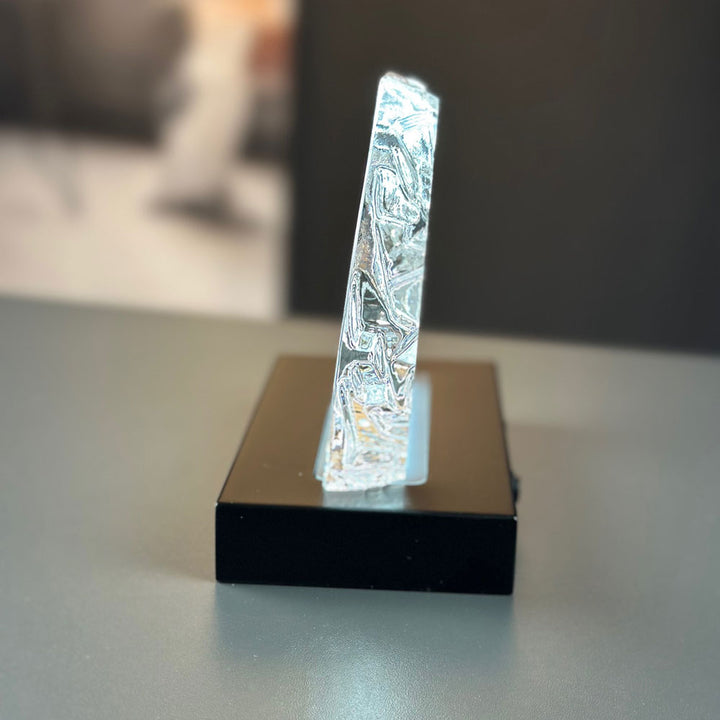 Isbergsformad glasblock sedd från sidan på mattsvart lyxljusbas
