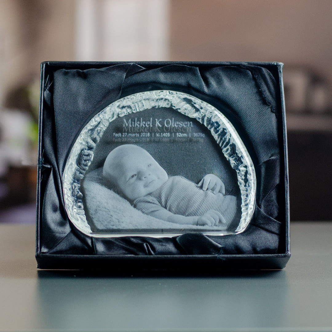 Liten isbergsformad glasblock med graverad bebis i svart presentask