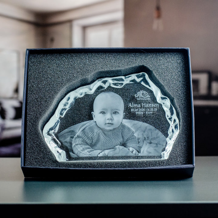 Isbergsformad glasblock med graverad bebis i svart presentask